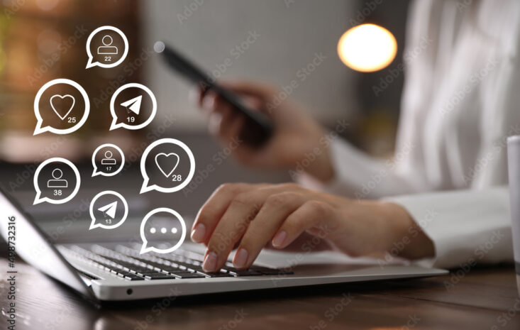 Different virtual icons and young woman using laptop and smartphone at table indoors, closeup. SMM (Social media marketing) concept